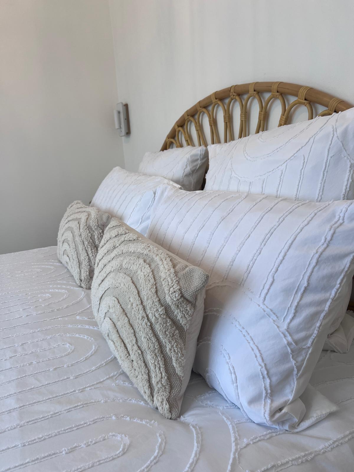 Linge de lit blanc aux textures naturelles et coussins en fibres douces, dans une chambre apaisante chez Origines be holistic.